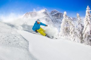 Skier skiing downhill in high mountains during sunny day.